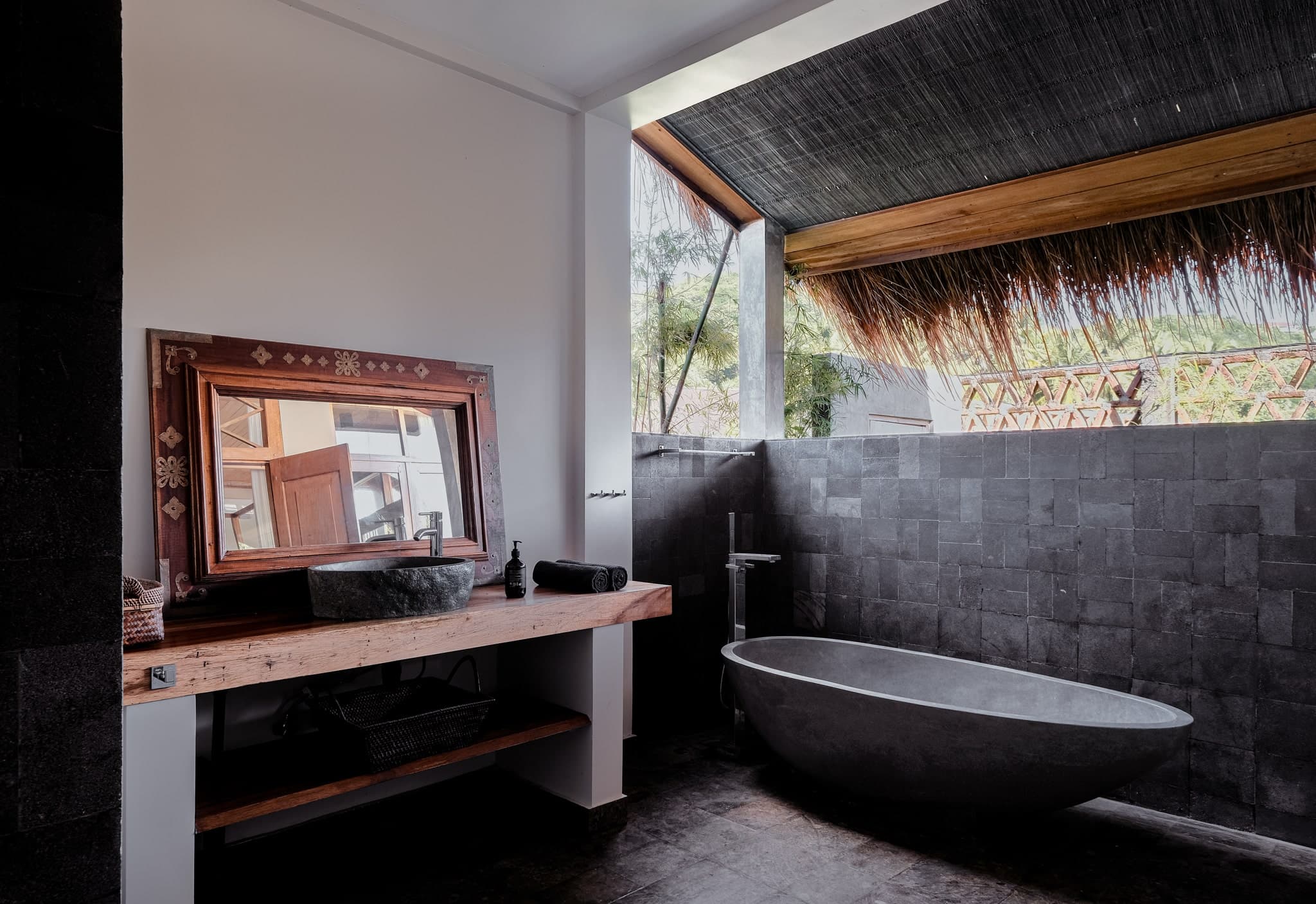 Luxury semi-outdoor bathroom at Villa Gudea in Lombok, Indonesia – Featuring a freestanding stone bathtub, rustic wooden vanity with stone sink, and tropical views for a spa-like experience