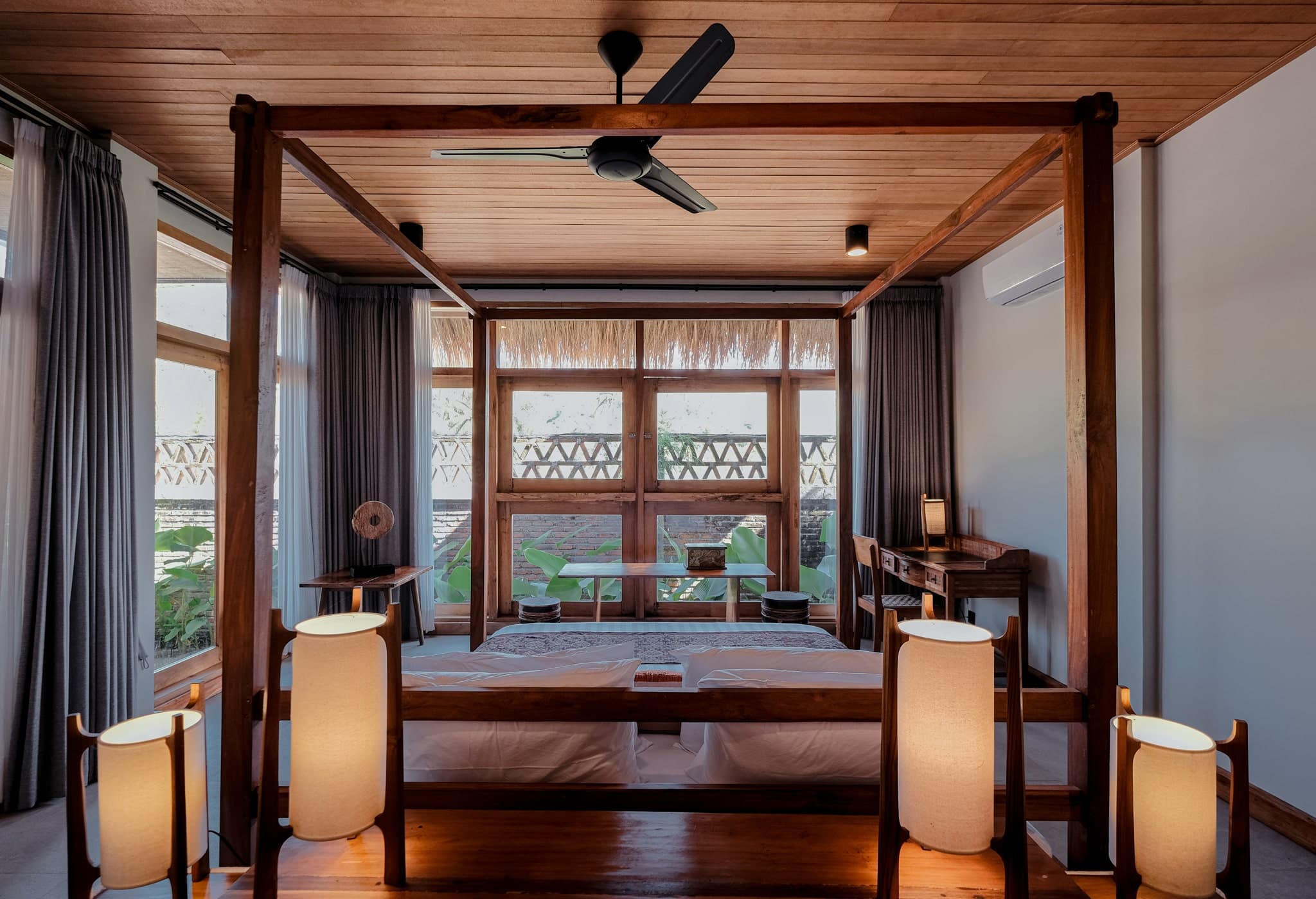 Elegant bedroom at Villa Gudea in Lombok, Indonesia – Featuring a wooden four-poster bed, floor-to-ceiling windows, tropical garden views, and a serene, luxurious design for a peaceful retreat