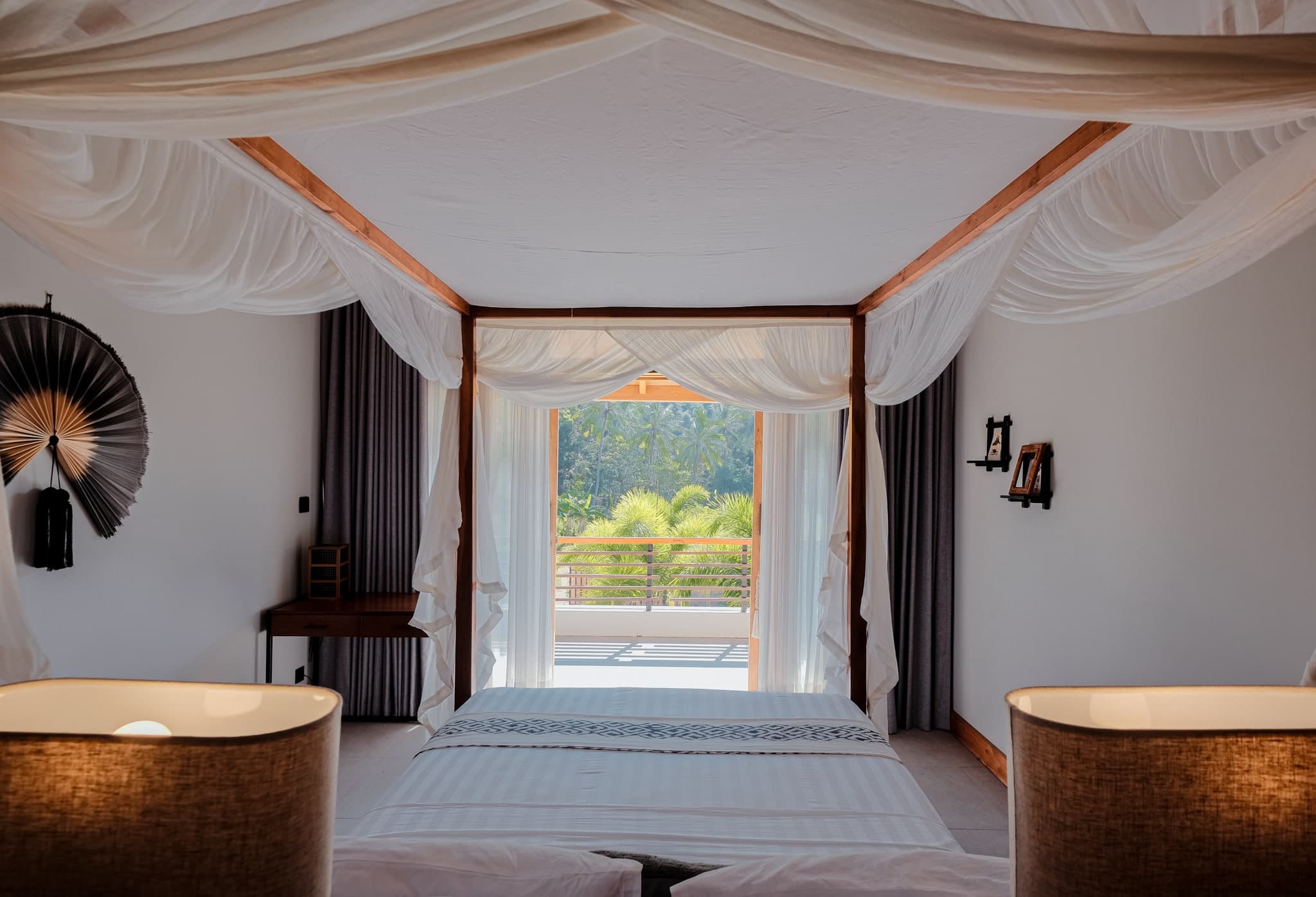 Luxurious bedroom at Villa Gudea, Lombok — Featuring a four-poster bed with flowing white curtains, a private balcony with lush tropical views, and elegant decor blending modern and traditional elements