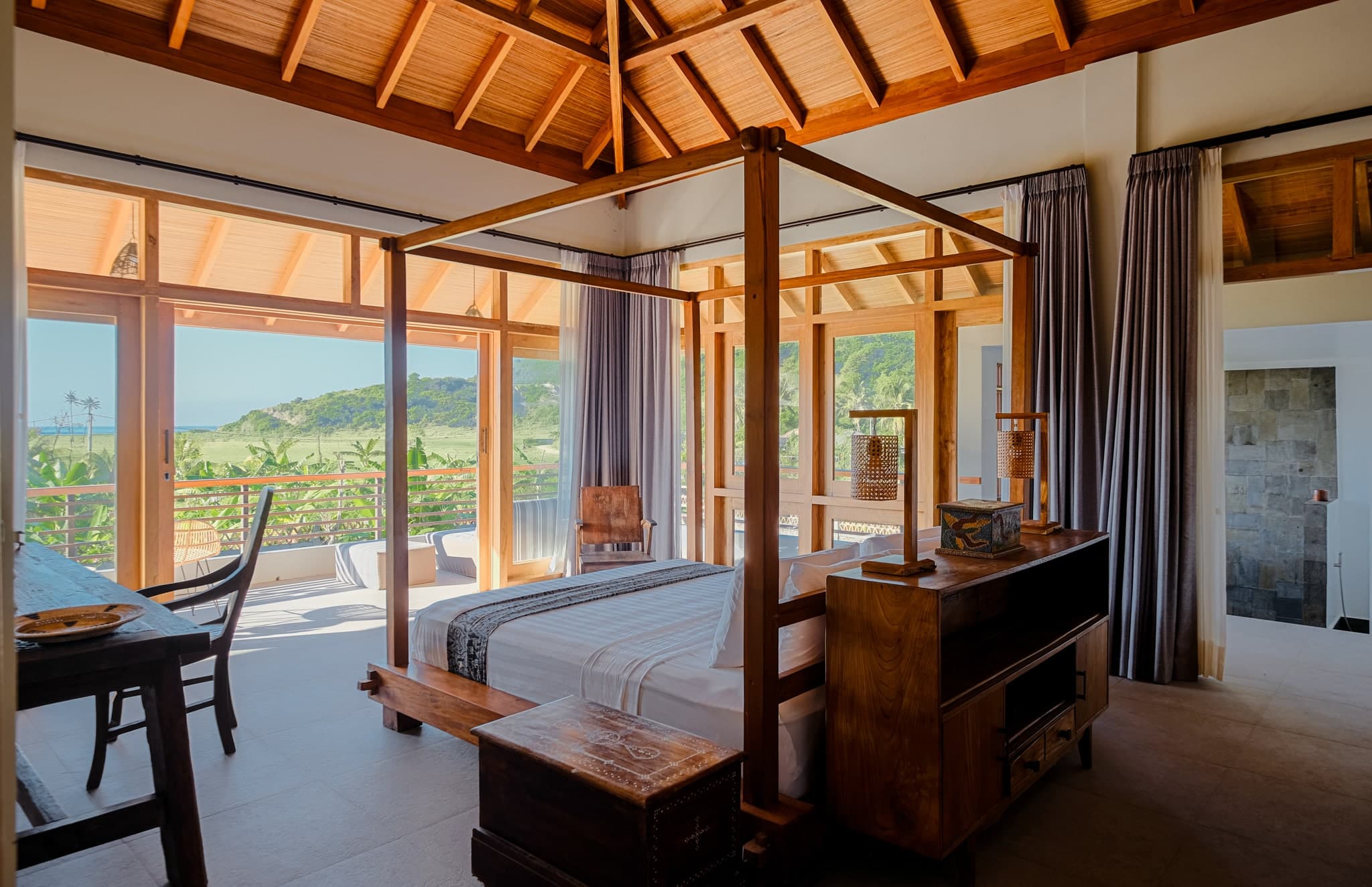 Spacious bedroom at Villa Gudea in Lombok, Indonesia – Featuring a wooden four-poster bed, vaulted ceiling, panoramic ocean and jungle views, and a private balcony for a luxury tropical getaway