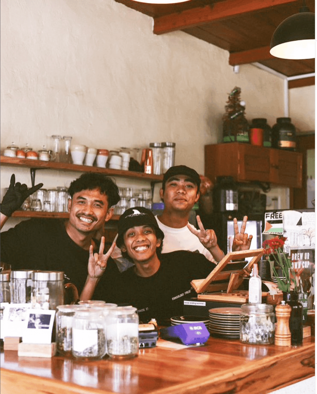 3 smiley baristas at a coffe place behind the counter